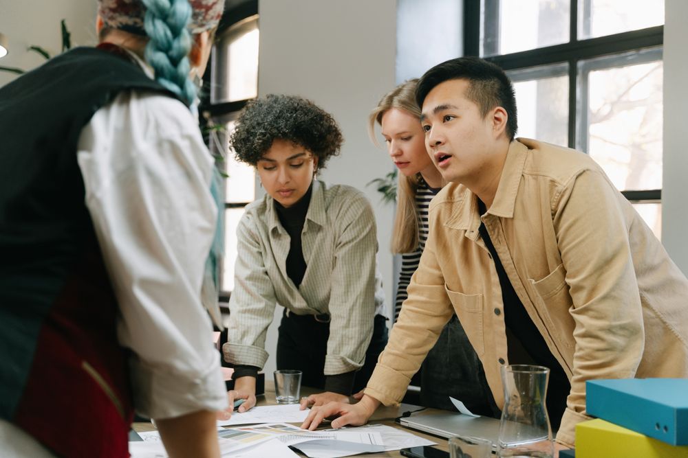 Tres colegas conversan sobre documentos alrededor de una mesa de trabajo