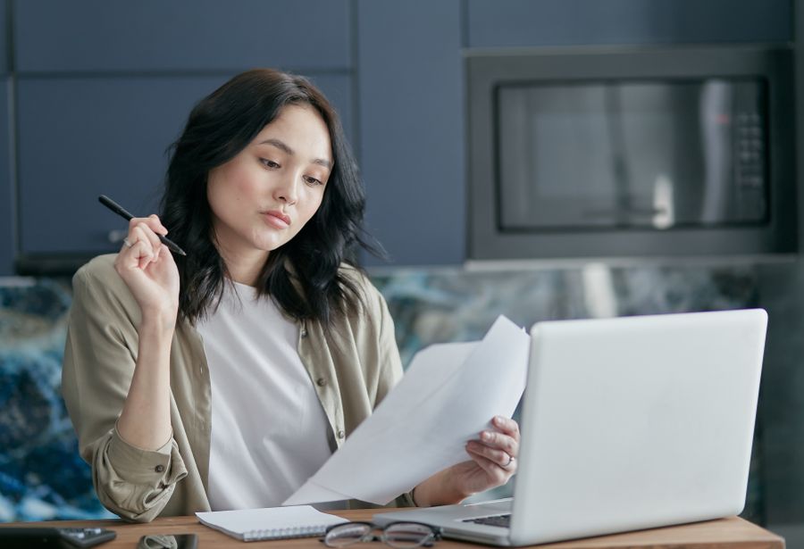 Una mujer revisa documentos impresos junto a su laptop